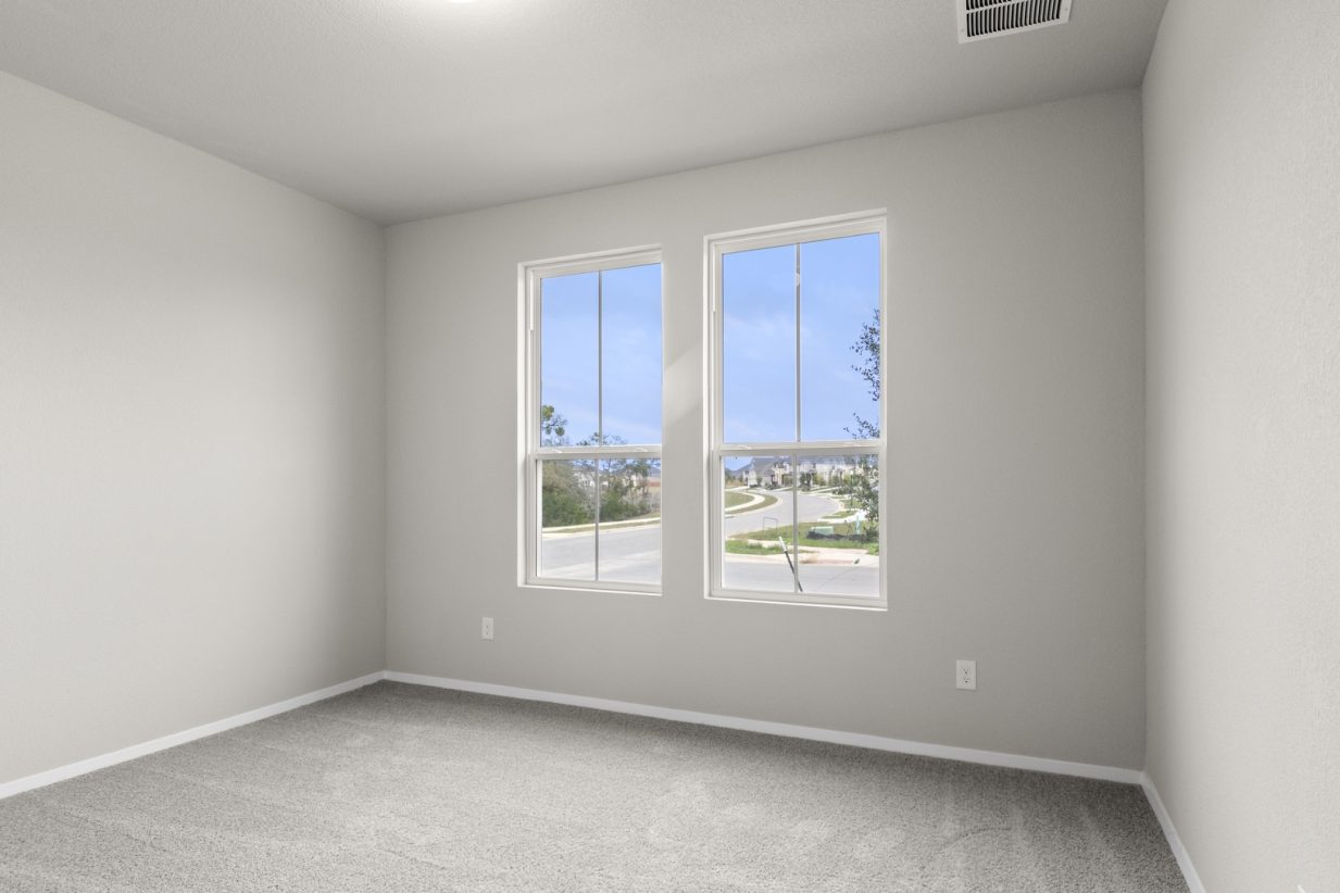 Image of a bedroom with tan carpeting and light grey walls and two large windows