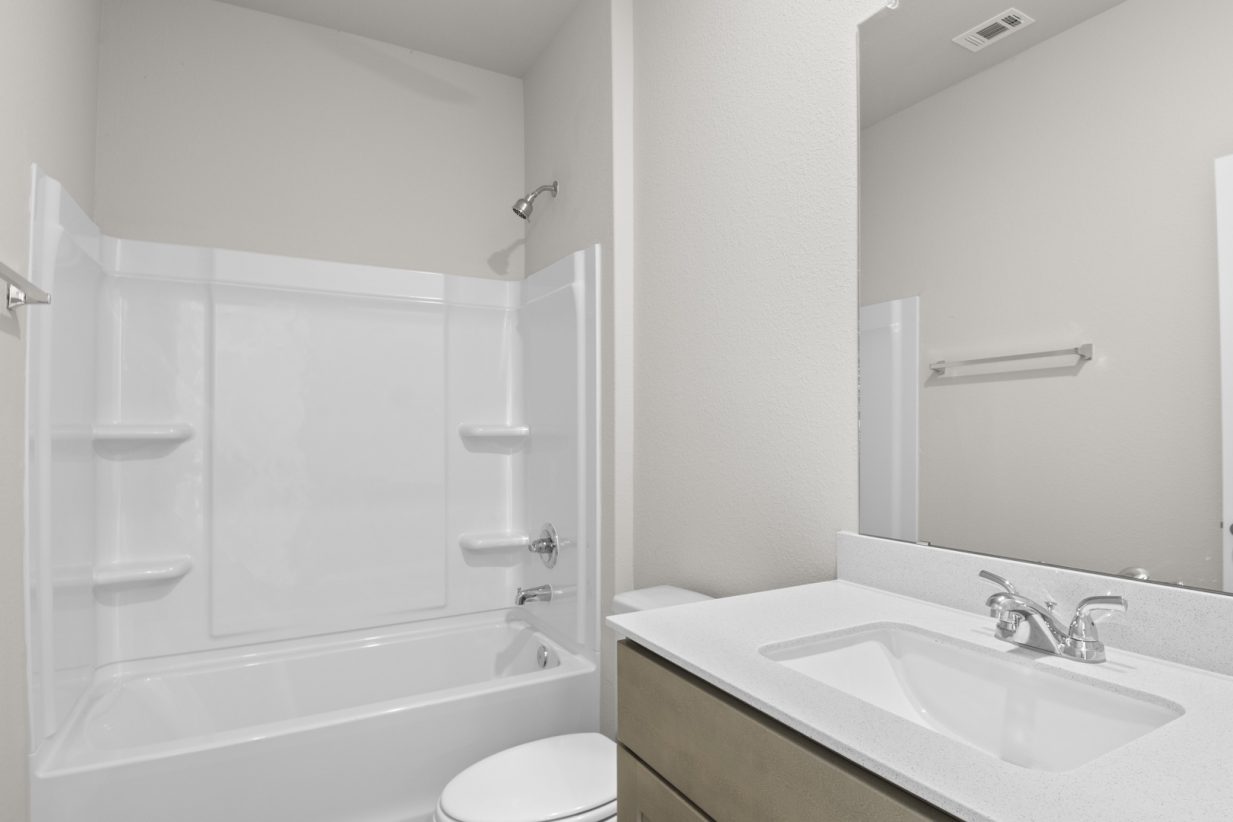 Image of a bathroom with a white vinyl walk-in shower, light brown cabinets, and a white vanity with a large mirror