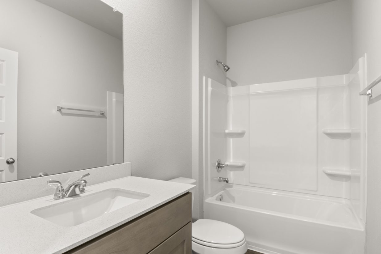 Image of a bathroom with brown cabinets, a white vanity, a large mirror, and a white vinyl walk-in shower