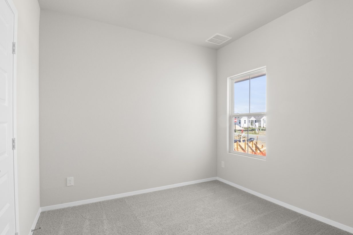 Image of a bedroom with tan carpeting, light grey walls and a window