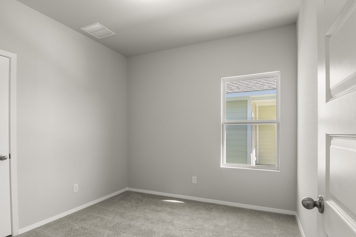 Image of a bedroom with tan carpeting, light grey walls and a window