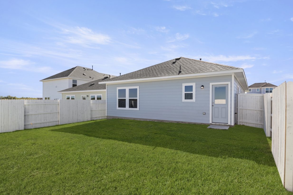 Image of a back exterior of a blue one-story home with a green grass backyard and a white wooden fence