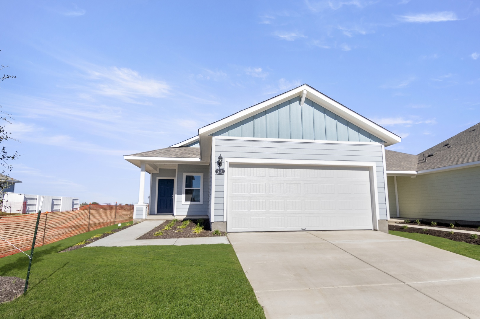 Image of a front exterior of a blue one-story home with a white garage door, white trim, a cement driveway and a dark blue front door
