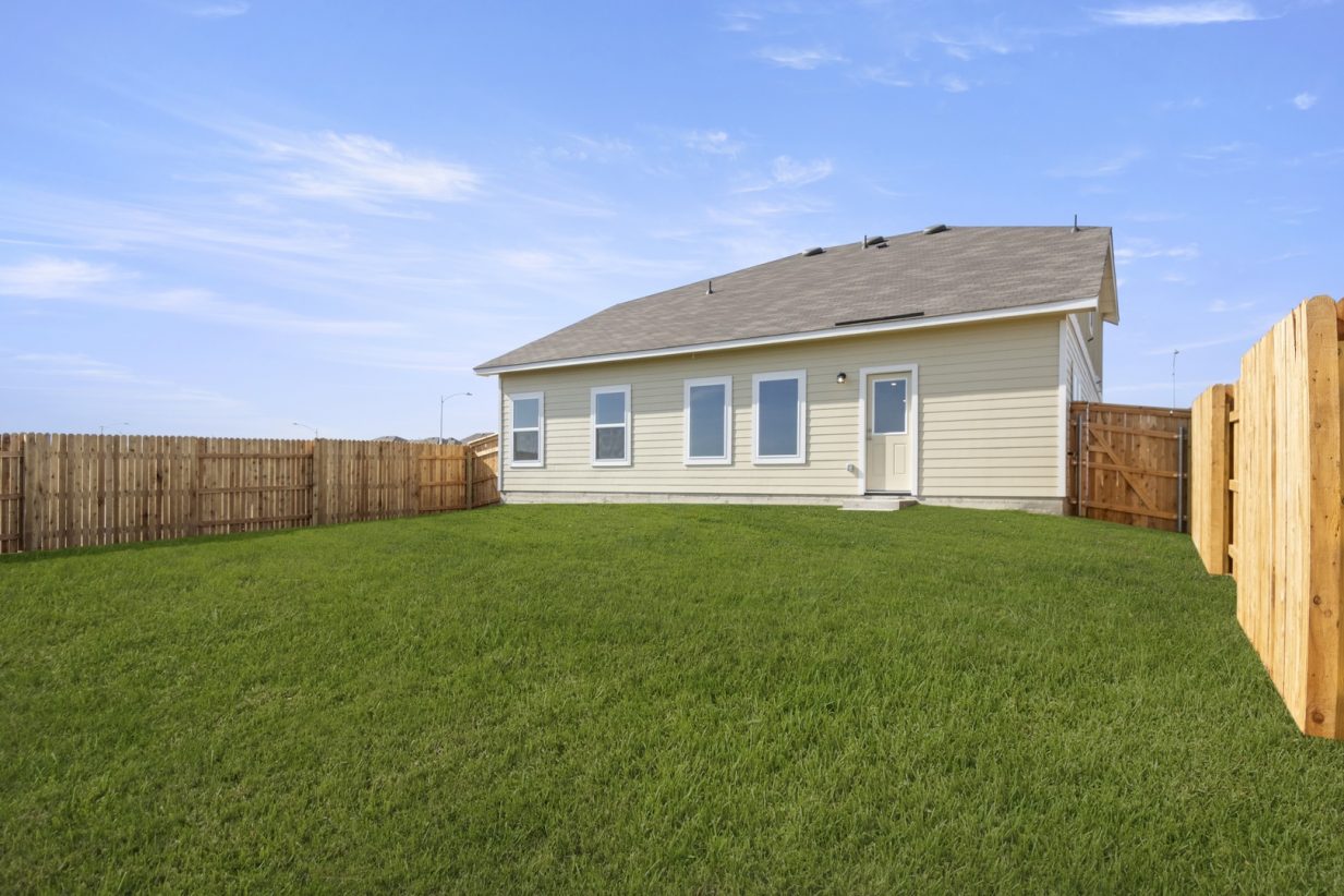Image of the back exterior of a tan two story home with a green grass backyard and a wooden fence