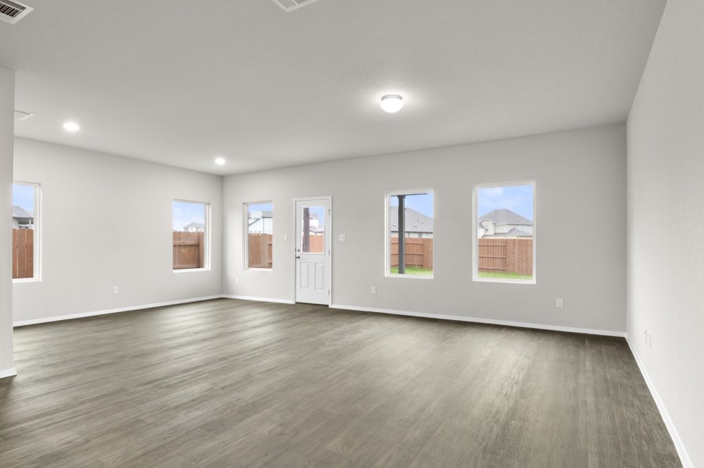Image of a living room with dark vinyl flooring, light grey walls and windows on each wall