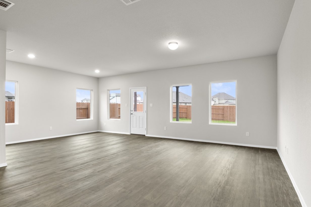 Image of a living room with dark vinyl flooring, light grey walls and windows on each wall