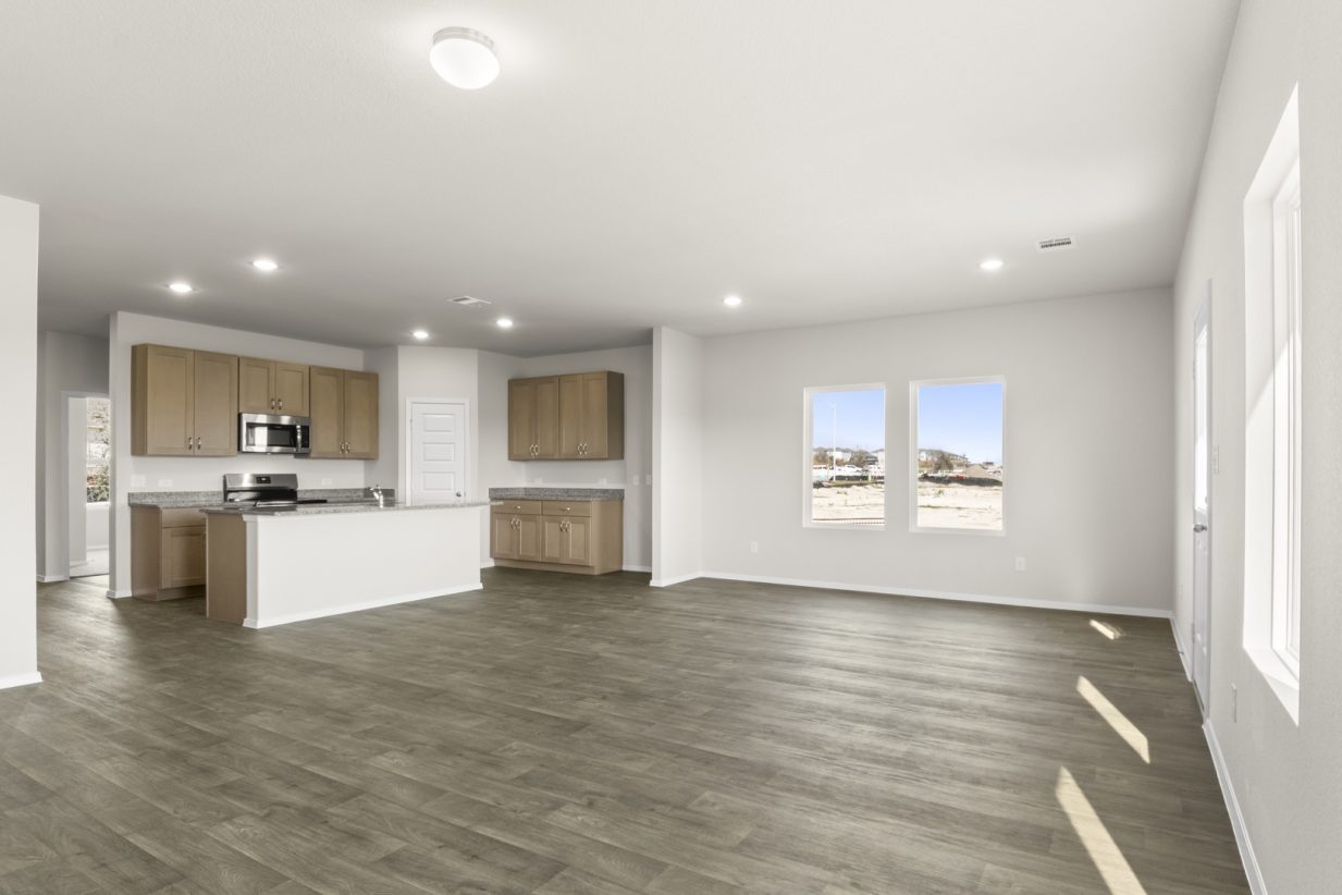 Image of a living room with light grey walls, brown vinyl flooring, and an open kitchen with a center island