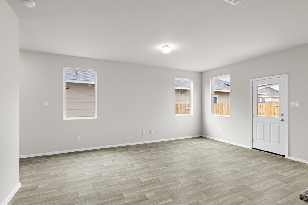 Image of a living room with cream walls, light brown flooring, windows, and a white back door