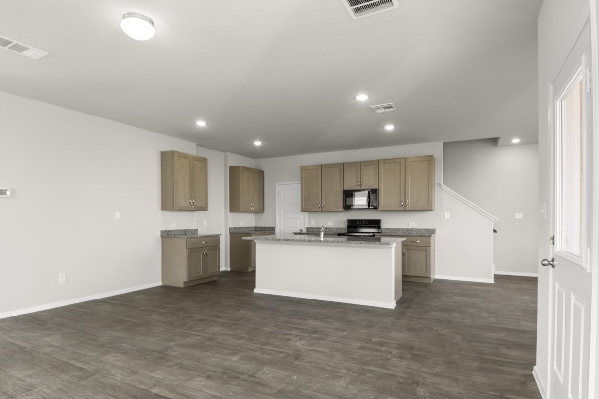 Image of a living room with grey walls, brown flooring, and a kitchen in the distance