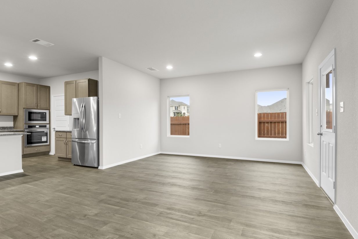 Image of a dining room with dark vinyl flooring, light grey walls and a connecting kitchen to the left
