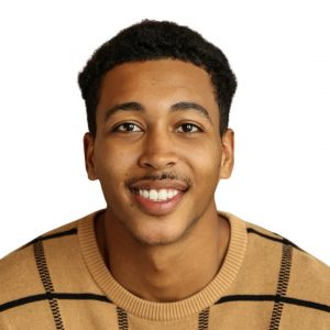 Headshot of smiling man wearing a tan and brown sweater