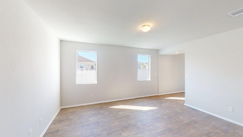 Image of a living room with dark wood-like flooring and light grey walls with two windows