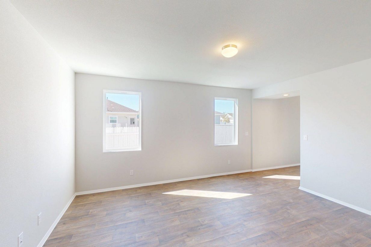 Image of a living room with dark wood-like flooring and light grey walls with two windows