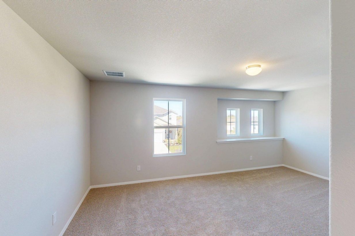 Image of a bedroom with tan carpeting and light grey painted walls with winodws
