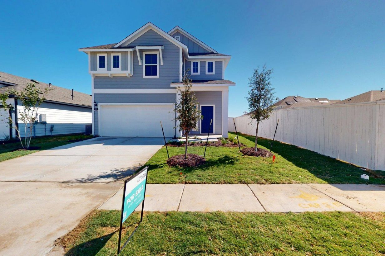 Image of the exterior of a blue two story home with a dark blue door and a cement driveway with a white two car garage