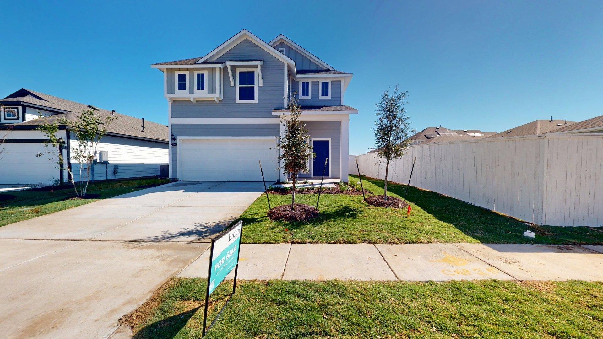 Image of the exterior of a blue two story home with a dark blue door and a cement driveway with a white two car garage