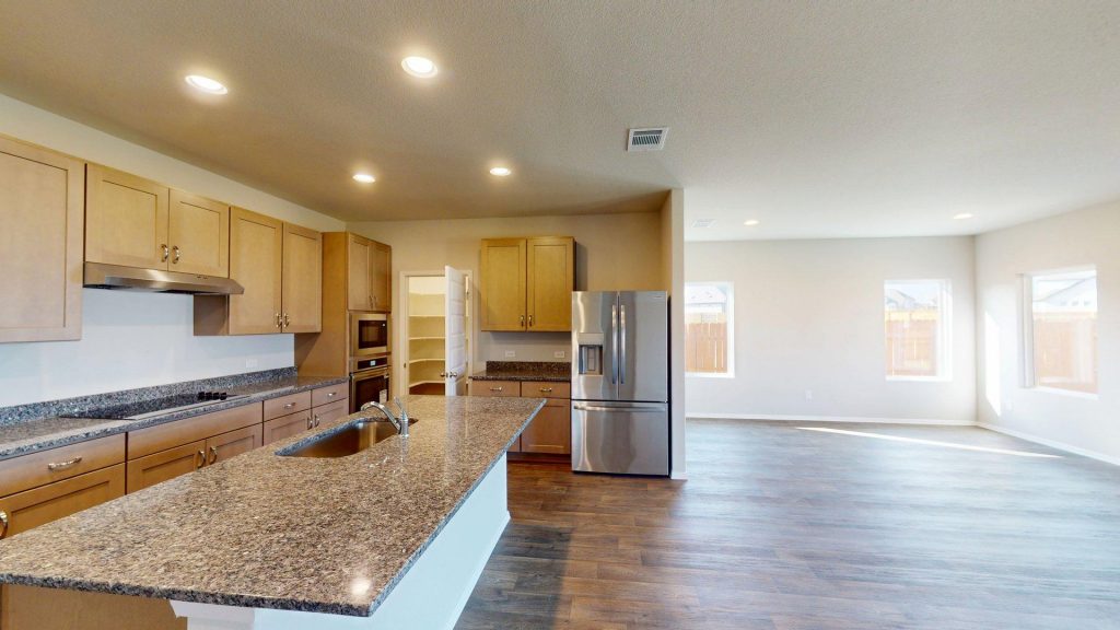 Matterport snapahot of a kitchen interior with a granite countertop center island, brown cabinets, stainless steel appliances, and a dining area