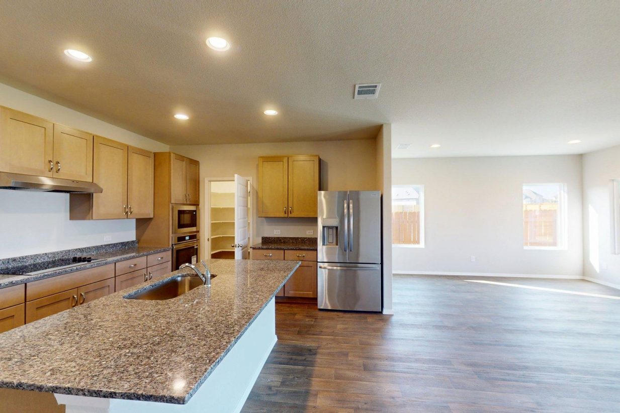Matterport snapahot of a kitchen interior with a granite countertop center island, brown cabinets, stainless steel appliances, and a dining area