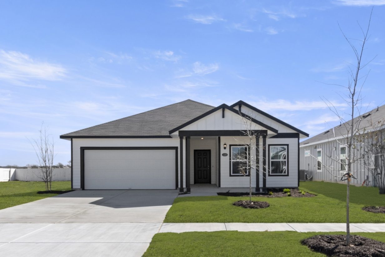 Image of a white one story house with black trim, a black front door, a cement driveway, a green grass front yard and a blue sky in the background
