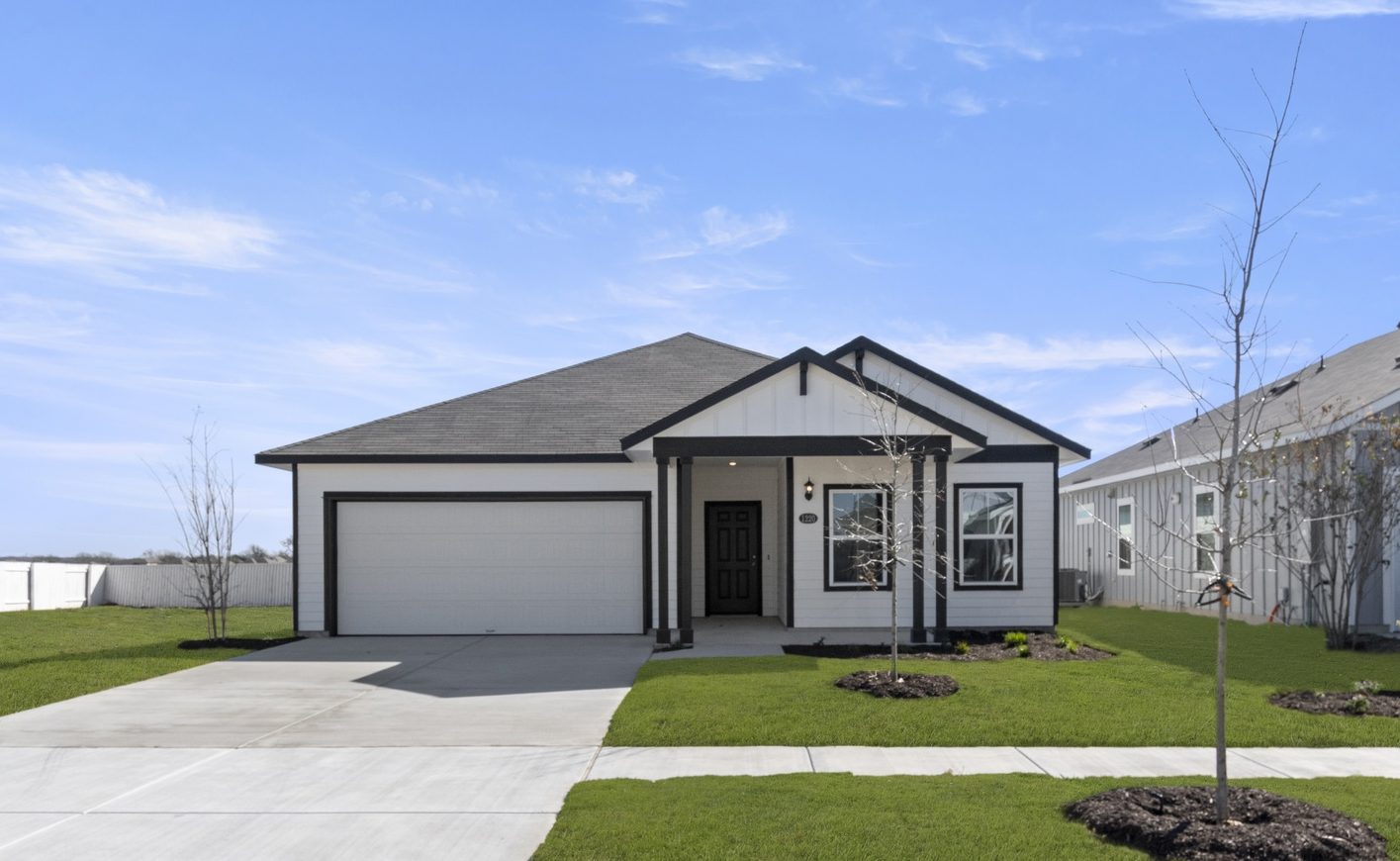 Image of a white one story house with black trim, a black front door, a cement driveway, a green grass front yard and a blue sky in the background
