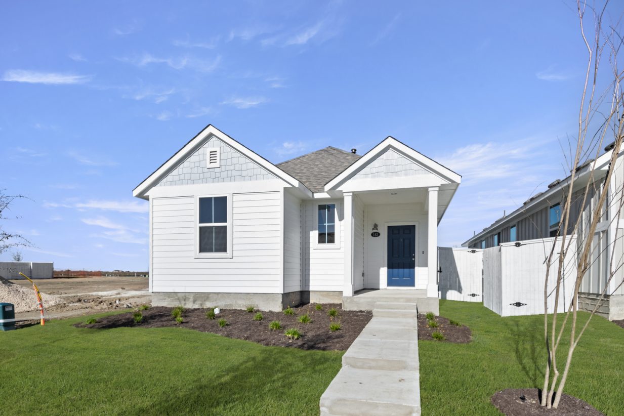 Image of a exterior of a one story white home with a light blue accent color with a dark blue front door and green grass