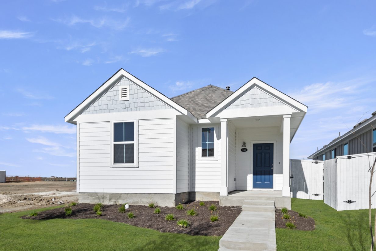 Image of a exterior of a one story white home with a light blue accent color with a dark blue front door and green grass