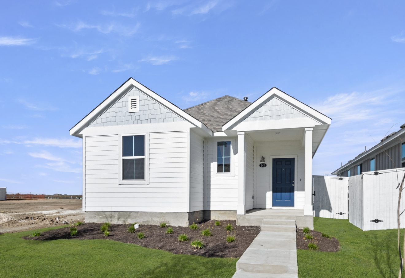 Image of a exterior of a one story white home with a light blue accent color with a dark blue front door and green grass