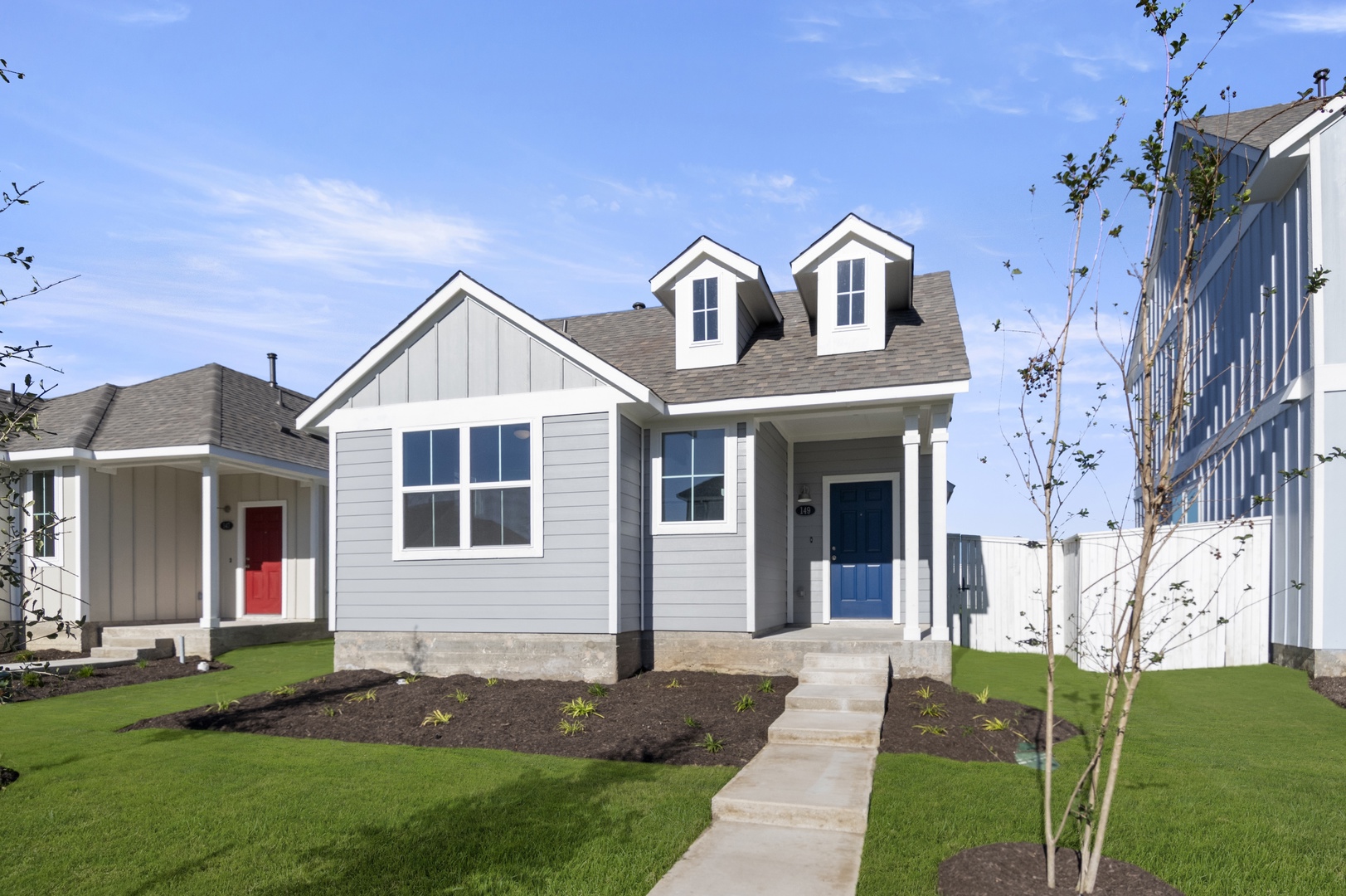 Image of the front exterior of a grey one story home with white trim, a blue front door, green grass and a blue sky in the background