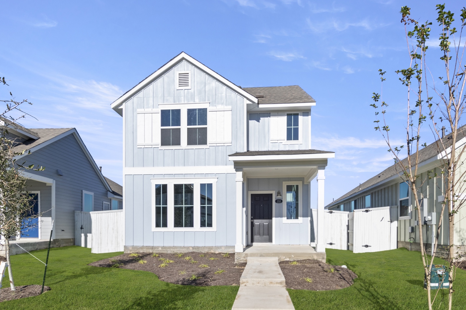 Image of the front exterior of a blue two story home with white trim, windows, and a brown front door with a cement front walkway