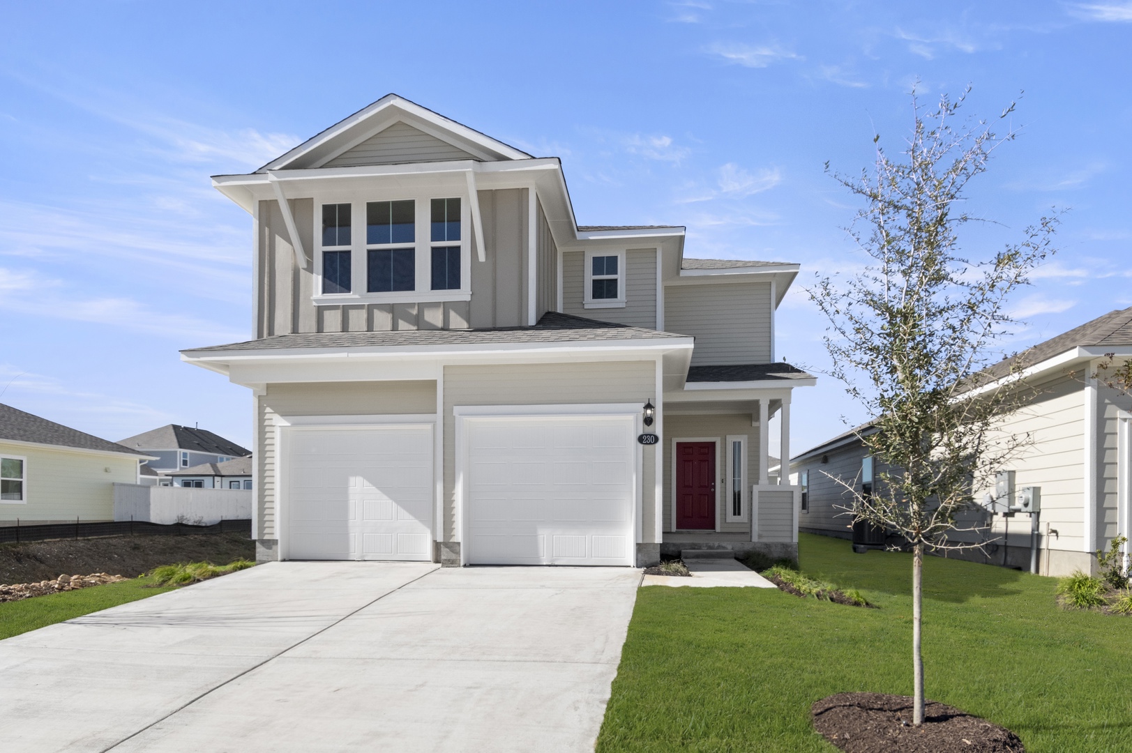 Image of the front exterior of a beige two story home with a double door two car garage with a cement driveway, white trim and a red front door
