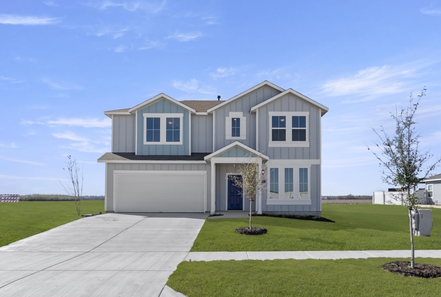 Image of a light blue two story house with white trim and garage door, a royal blue front foor, a cement driveway, green grass front yard and a blue sky in the distance