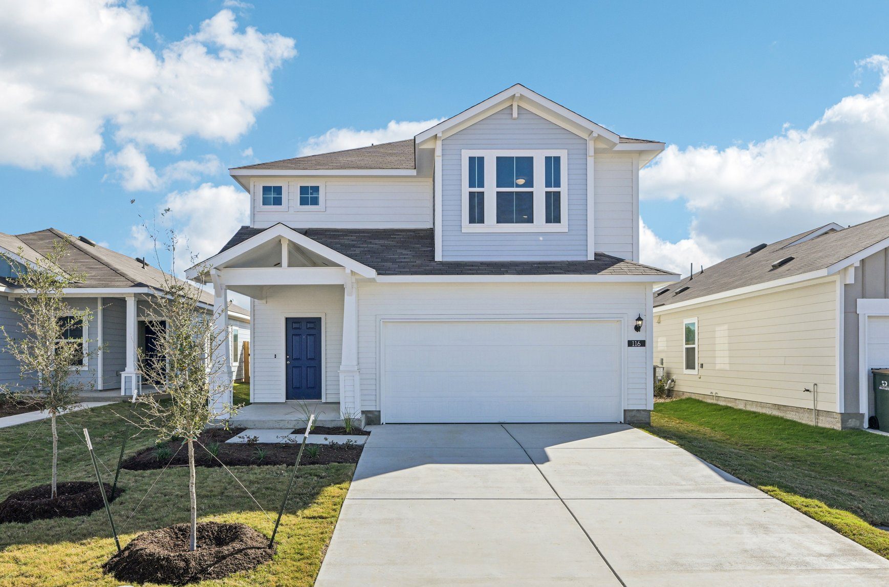 Image of a white and blue two story house with a garage, cement driveway, blue front door, green grass and a blue sky in the background