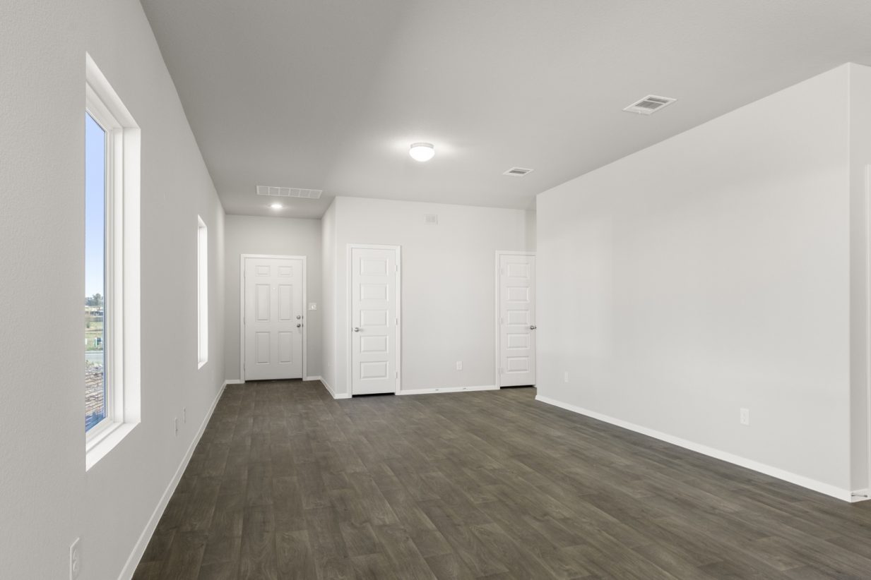 Image of a living room with dark brown floors, light grey walls, a white front door and windows