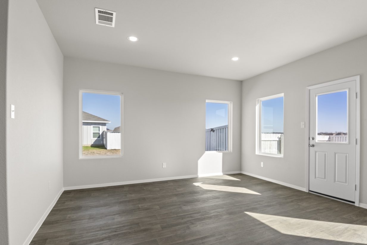 Image of a dining room with light grey walls, dark brown flooring, windows, and a white back door
