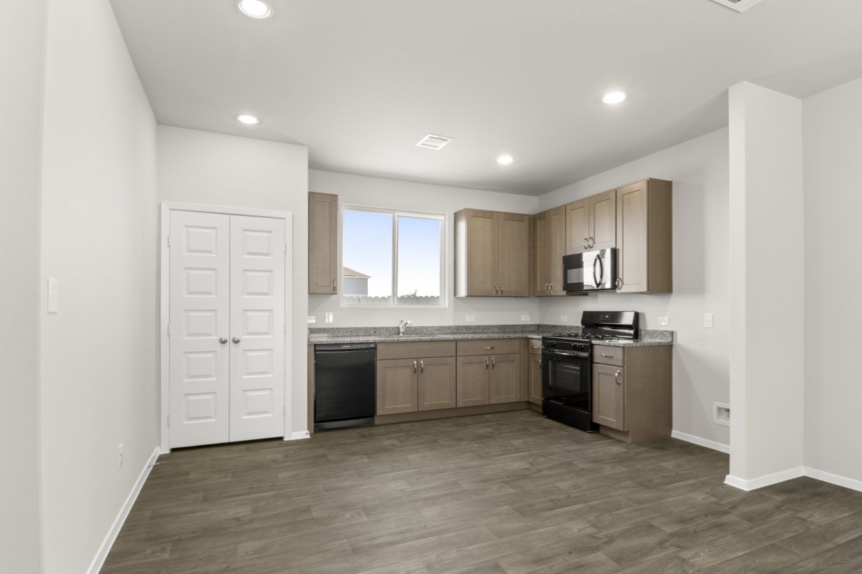 Image of a L-shaped kitchen with dark vinyl flooring, brown cabinets, granite countertops and black appliances