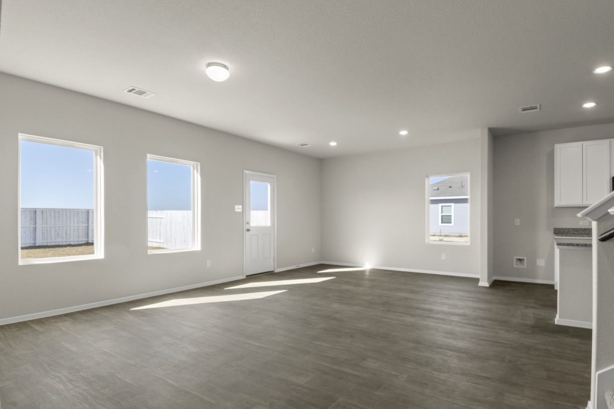 Image of a living room with cream walls, windows, a back door, dark brown flooring and white trim