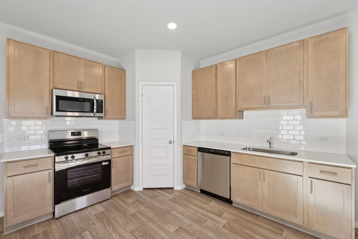 Image of a kitchen with a corner pantry, light brown cabinets, stainless steel appliances, white back splash and silestone countertops