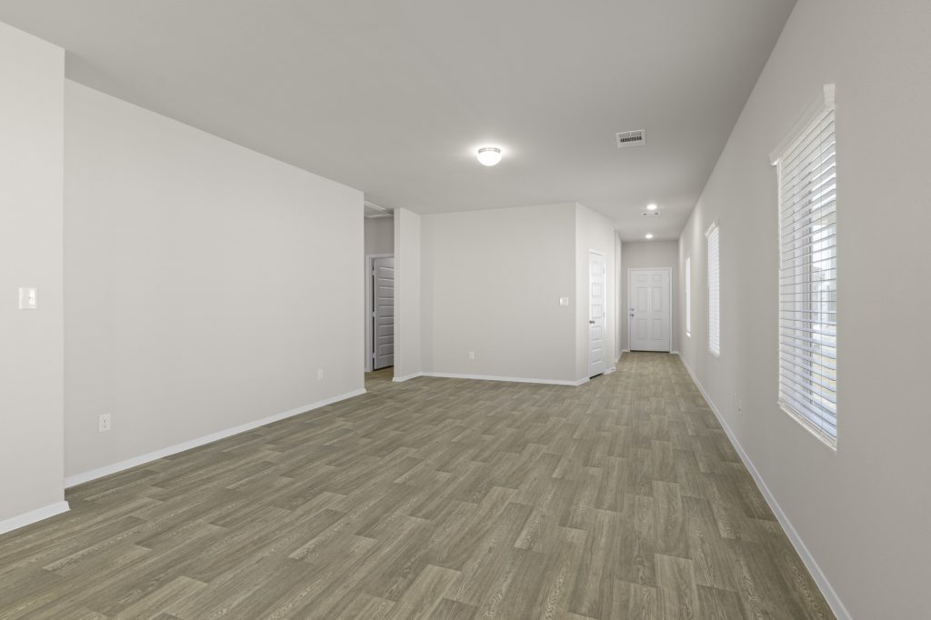 Image of a living room with beige walls, light brown wood-look flooring, and windows with blinds