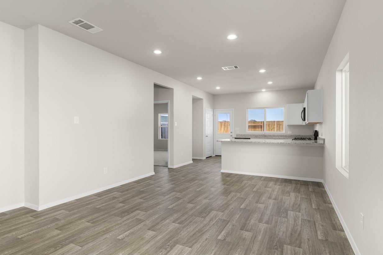Image of a dining room area with beige walls, windows, a connecting kitchen and a back white door