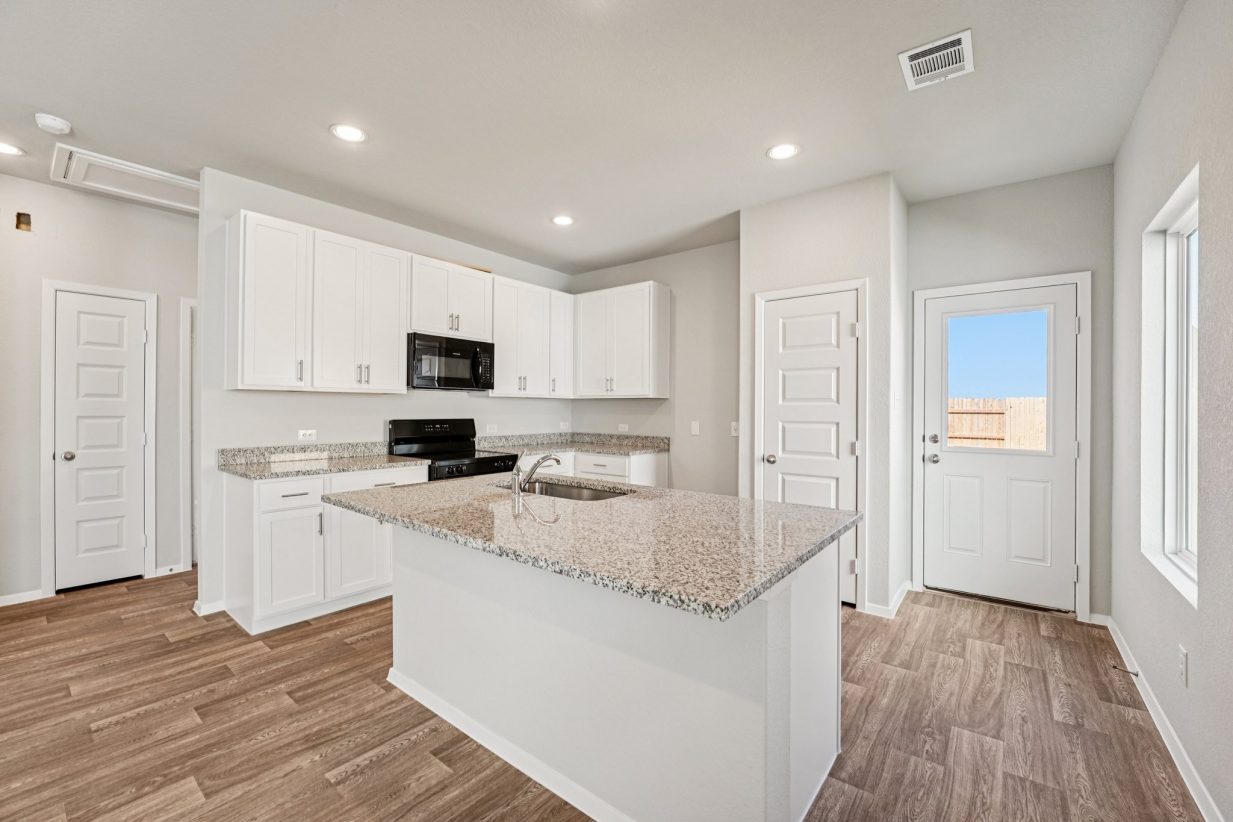 Image of a kitchen with white cabinets, center island, black appliances and a back door