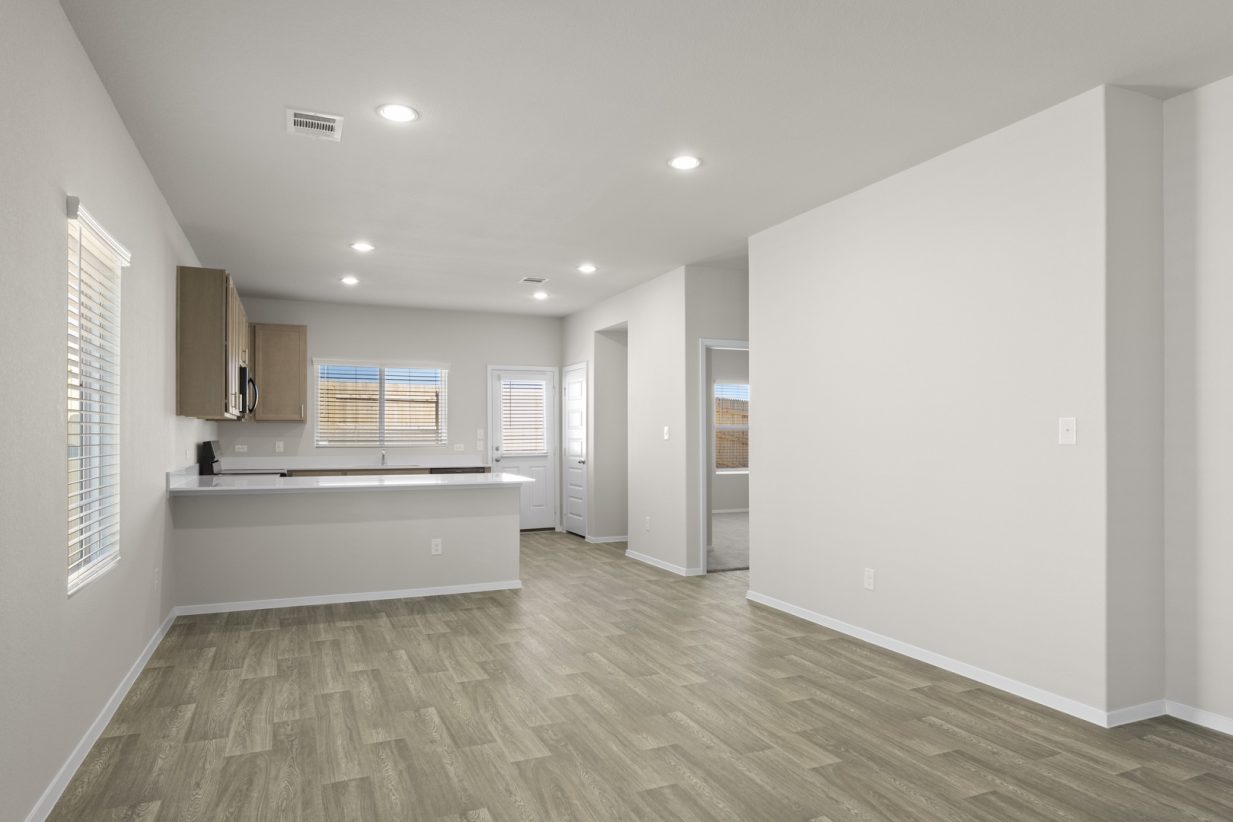 Image of a dining room with beige walls, light brown flooring, and an open U-shaped kitchen