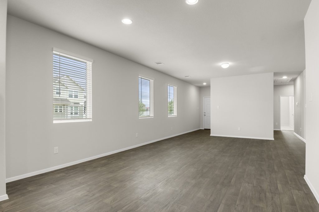 Image of a one-story home dining room with brown vinyl flooring, light grey walls, and windows
