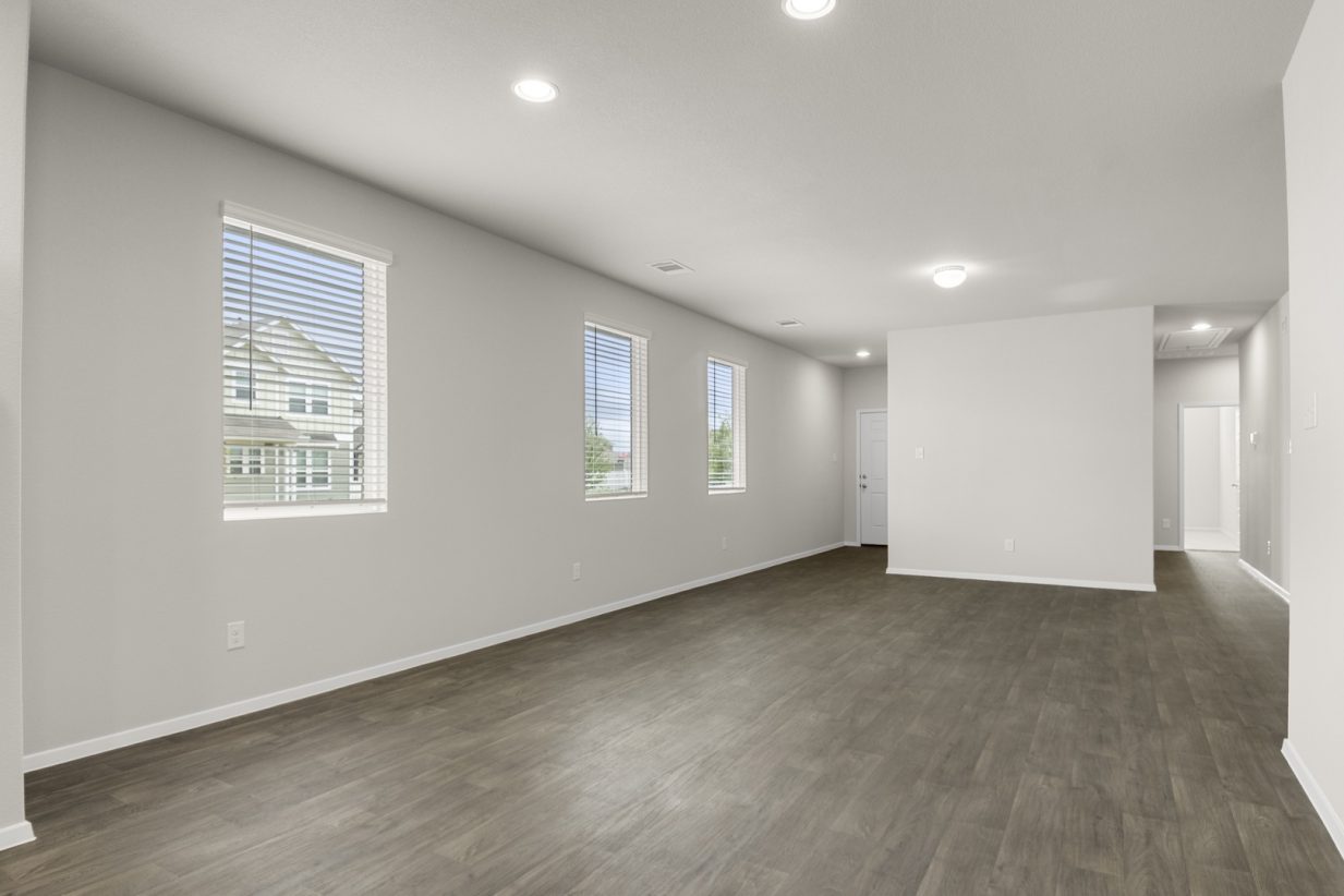 Image of a one-story home dining room with brown vinyl flooring, light grey walls, and windows