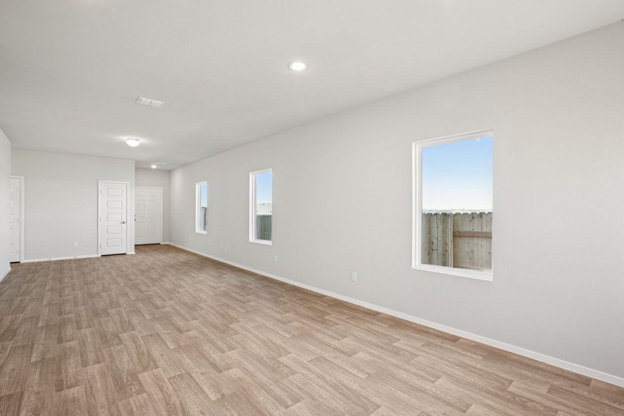 Image of a living room with light grey walls, vinyl flooring, windows, and white trim