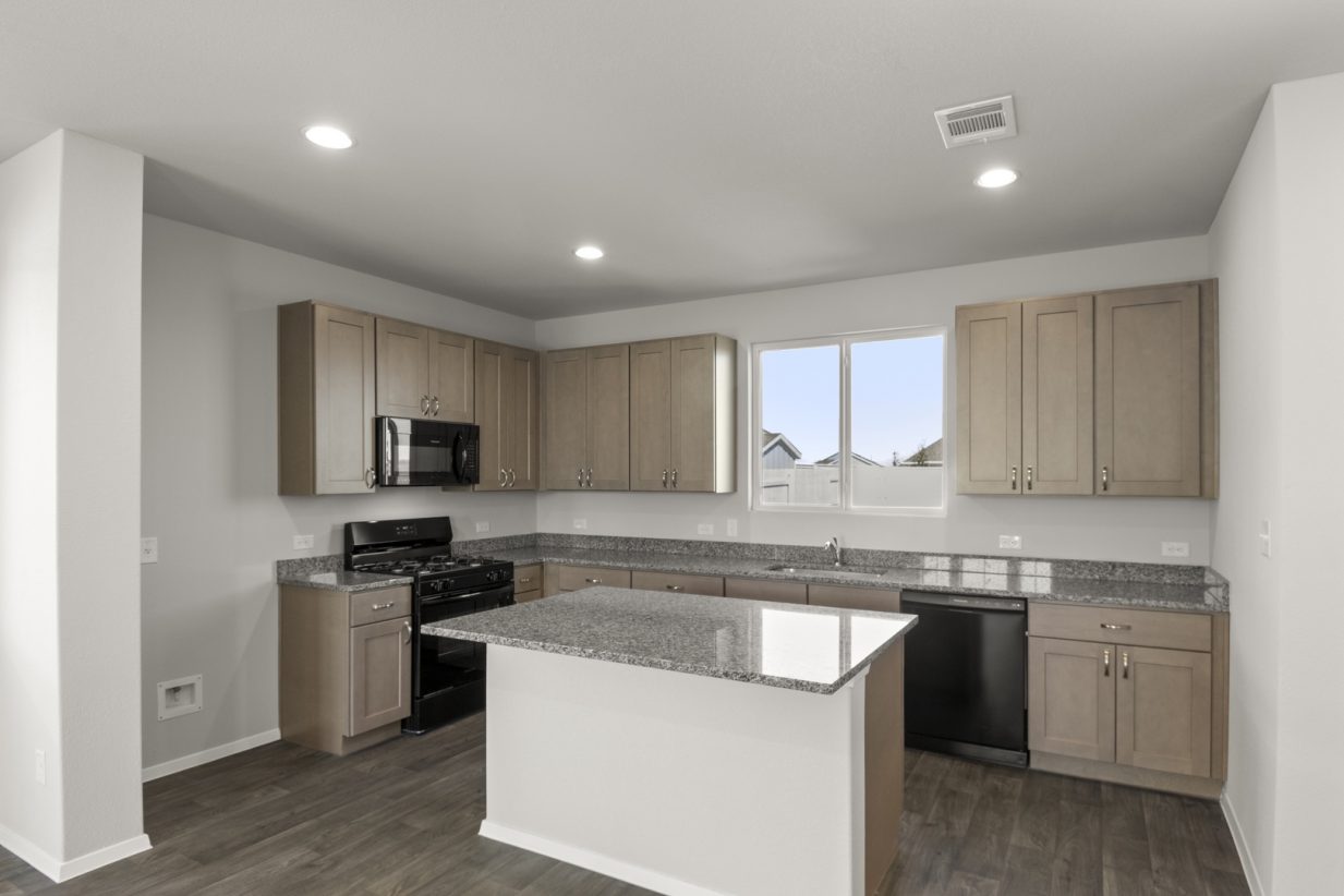Image of a kitchen with a granite counter top center island, light brown cabinets, black appliances and a window above the sink