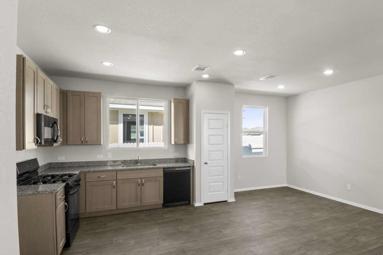 Image of a kitchen and dining room area with an L-shaped kitchen, dark. brown vinyl flooring, light grey walls and a window