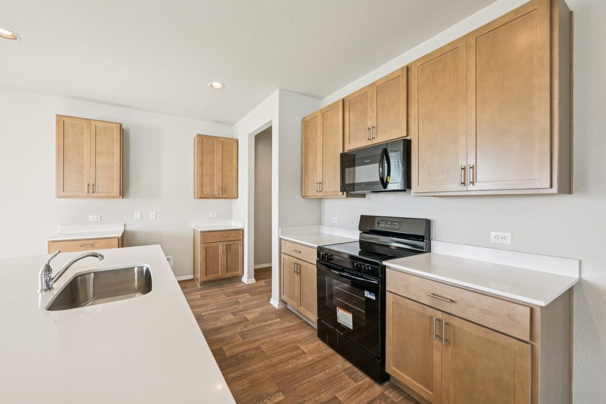 Image of a kitchen with brown cabinets, black appliances and a center island