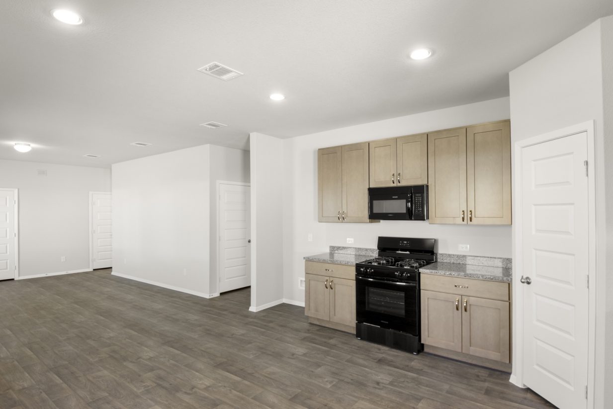 Image of a L-shaped kitchen with light brown cabinets, granite countertops, and black appliances
