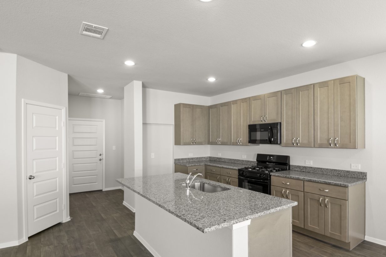 Image of a kitchen with light brown cabinets, granite countertops, black appliances and a center island