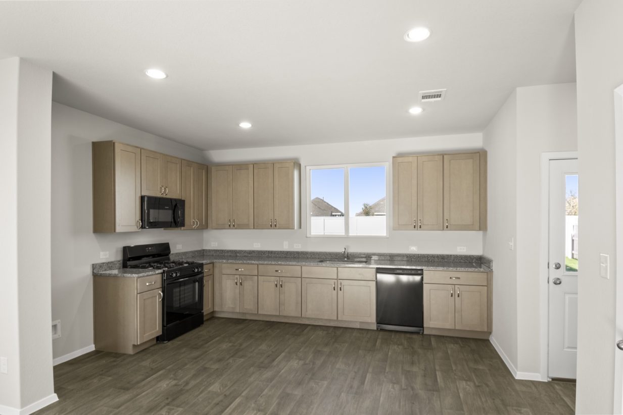 Image of a kitchen with light brown cabinets, granite countertops, black appliances and dark vinyl flooring